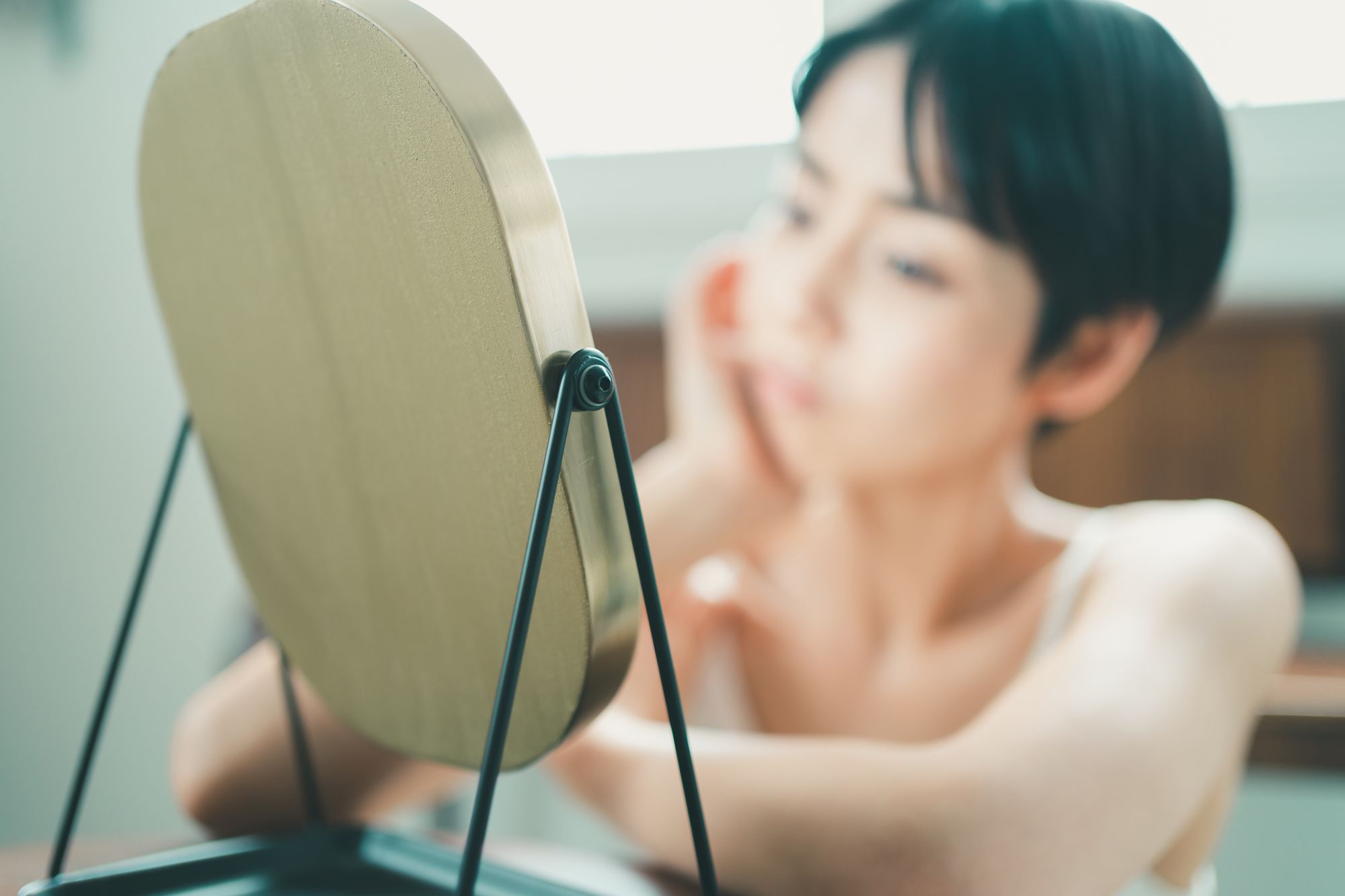 鏡を見て頬杖をつくショートカットの女性