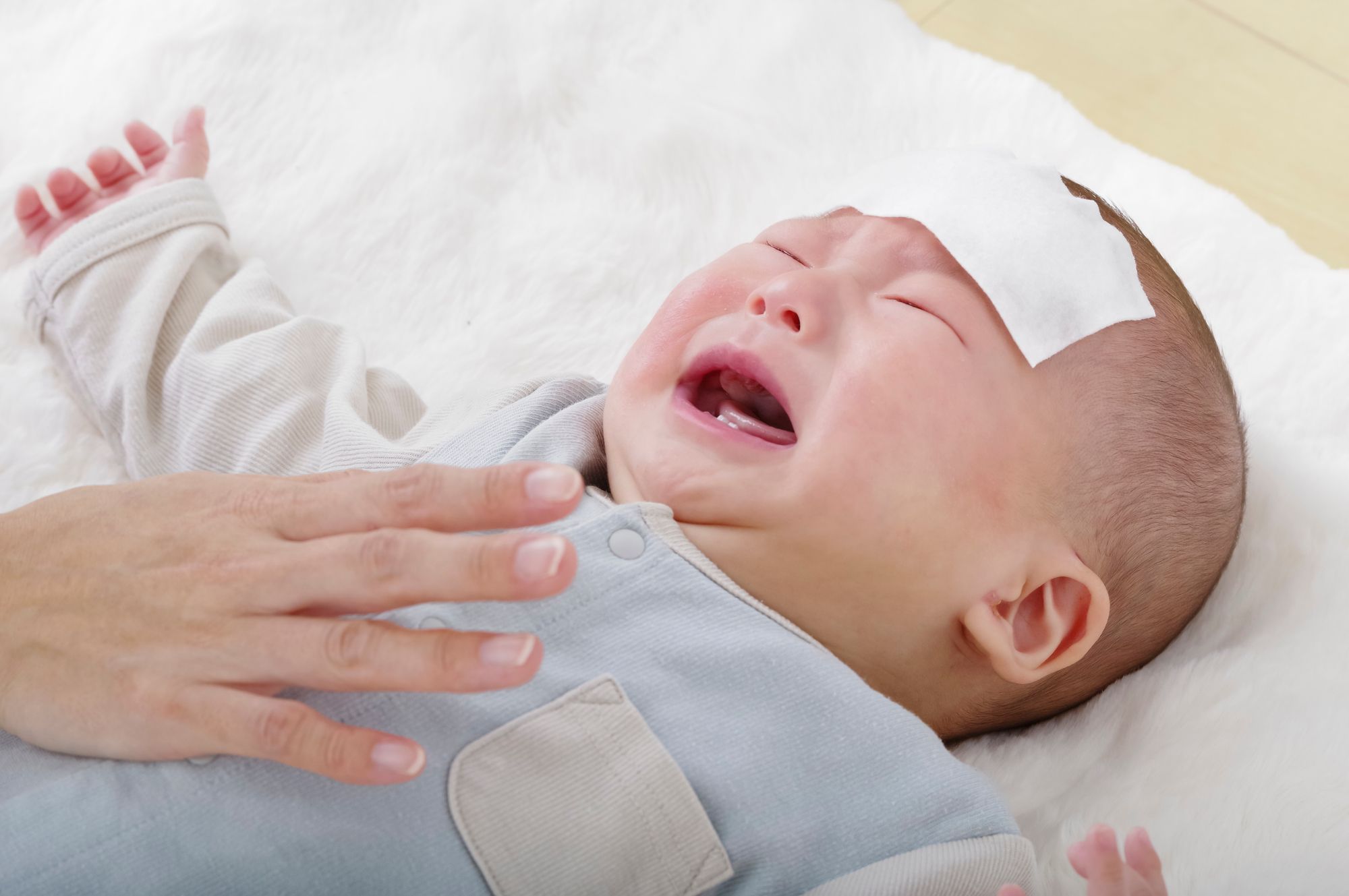 おでこに冷却シートを貼って泣く赤ちゃん