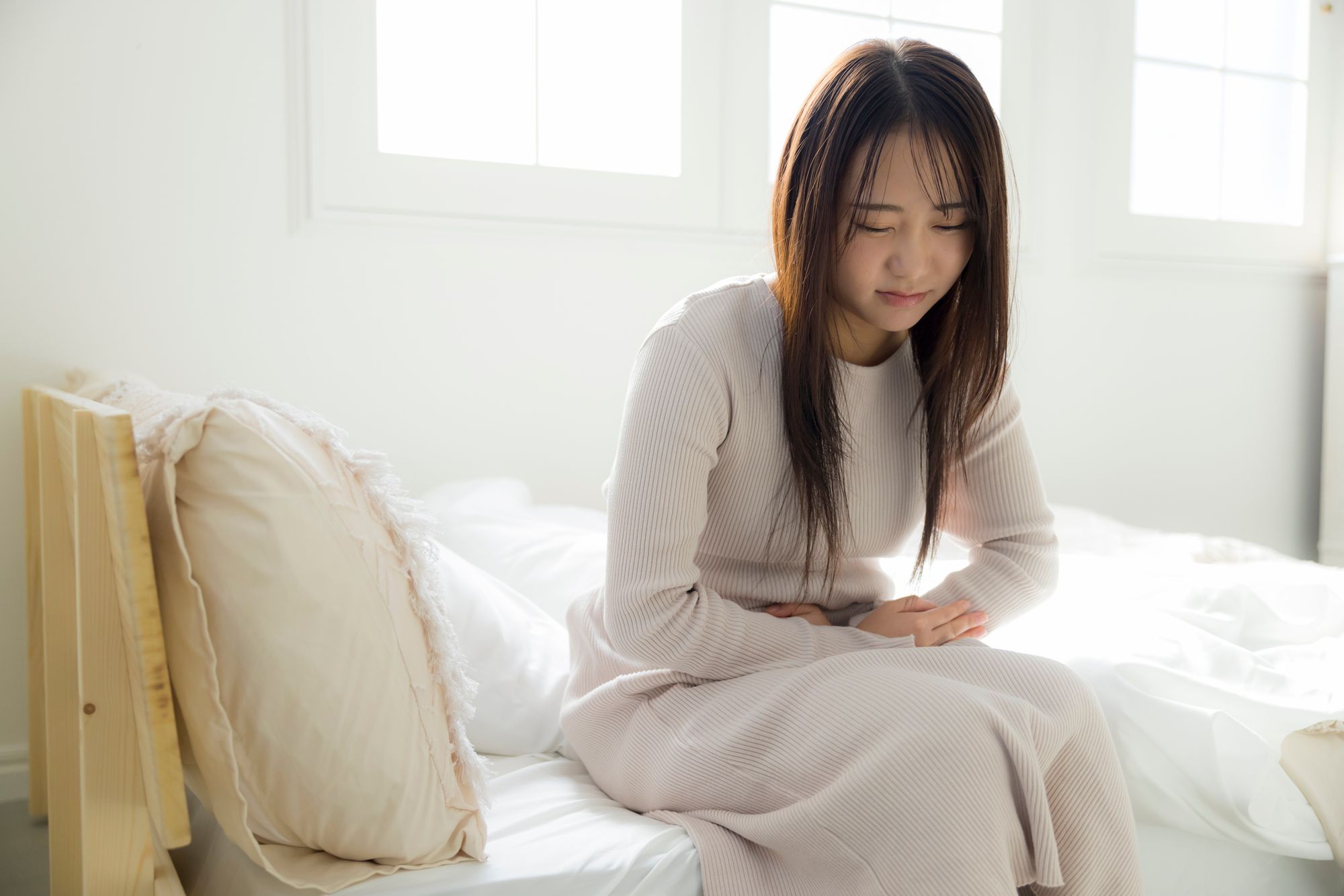 腹痛でお腹を抱えてベッドに座る女性