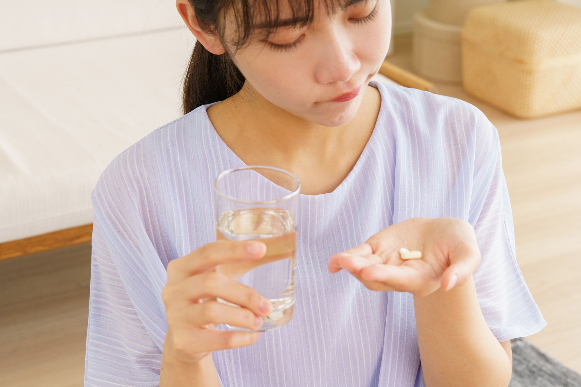 コップの水と薬を持って、困った顔をする女性