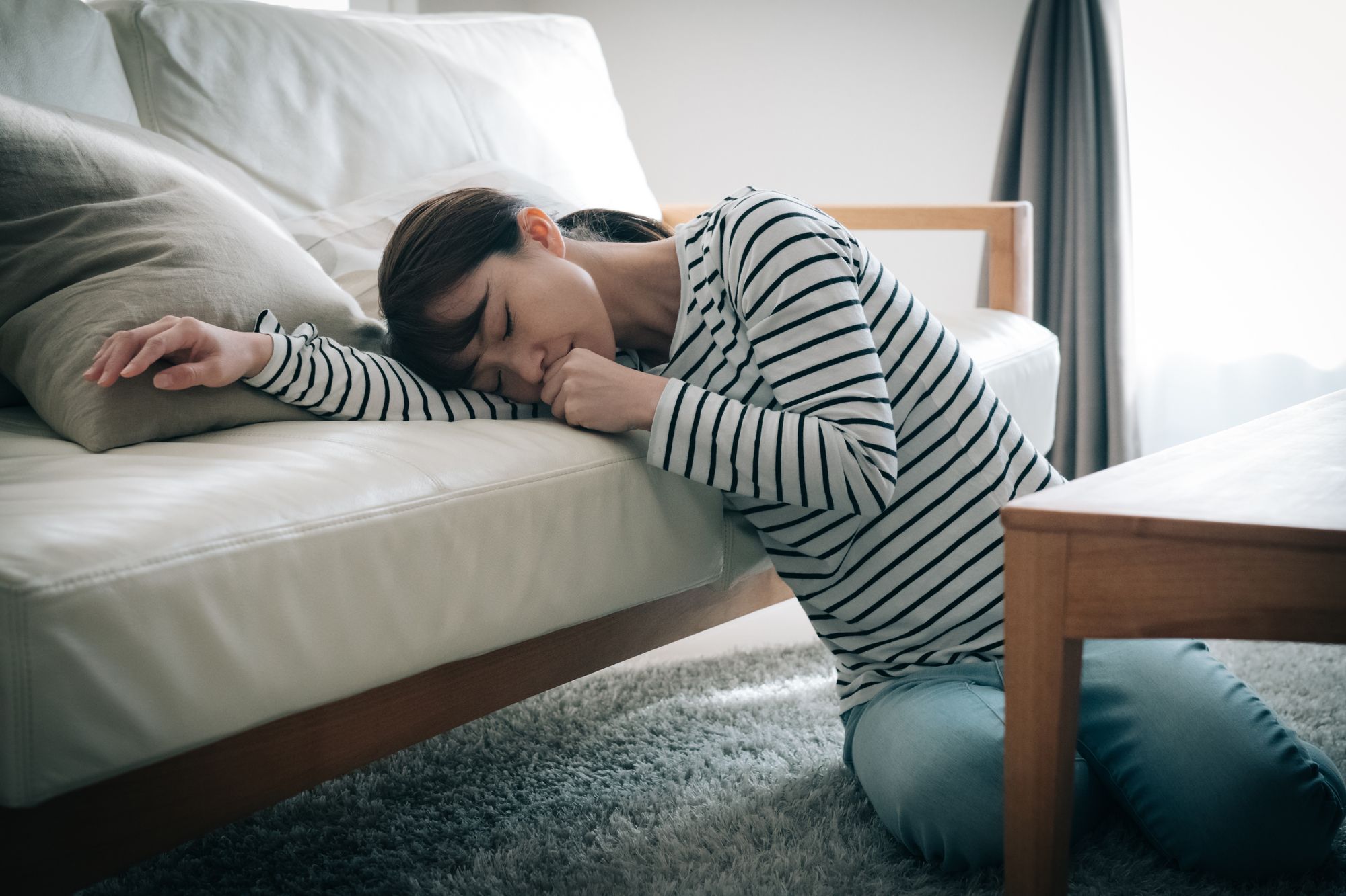 つわりの気持ち悪さでソファーに倒れこむ女性