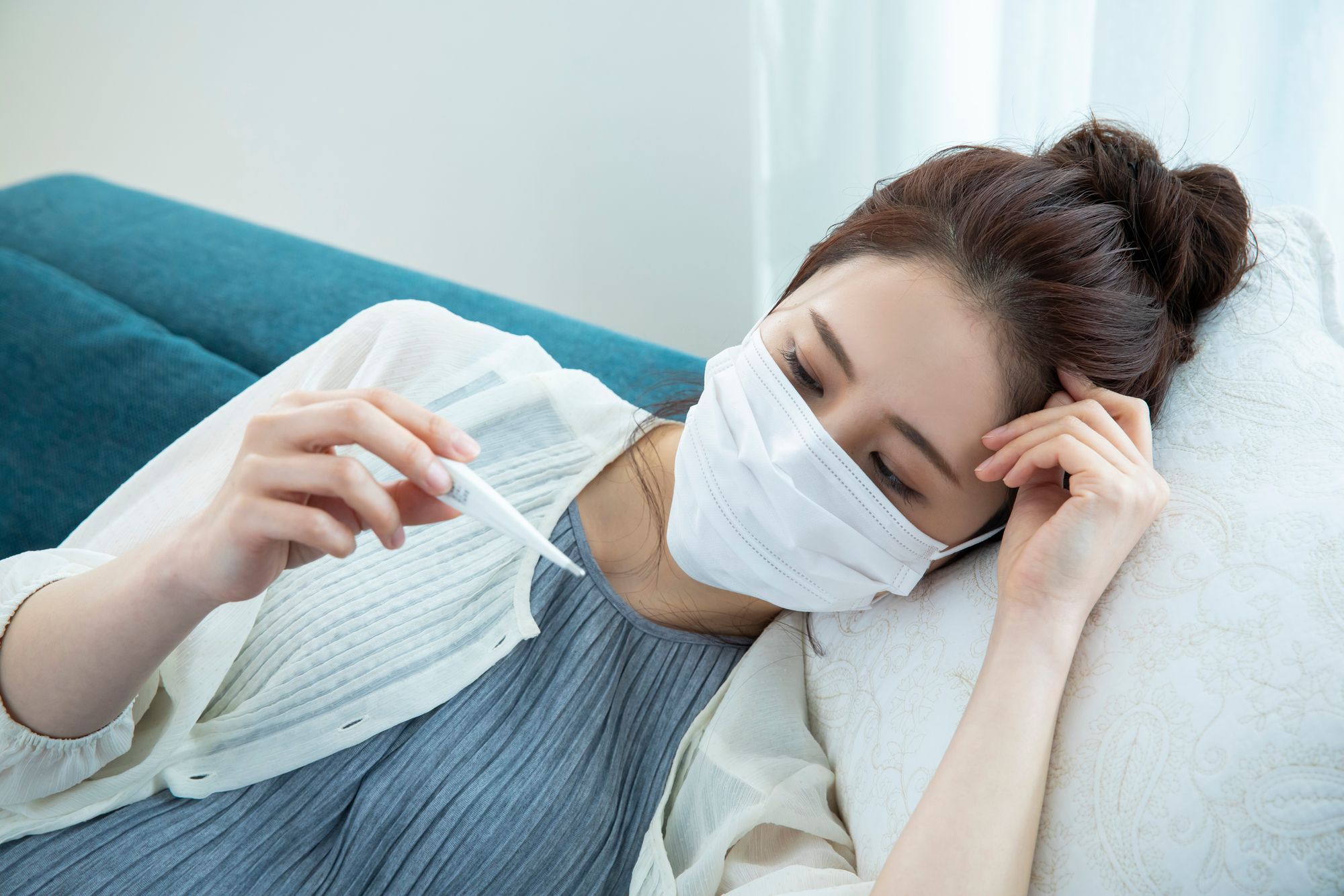 ソファーに横になり、熱を測る女性