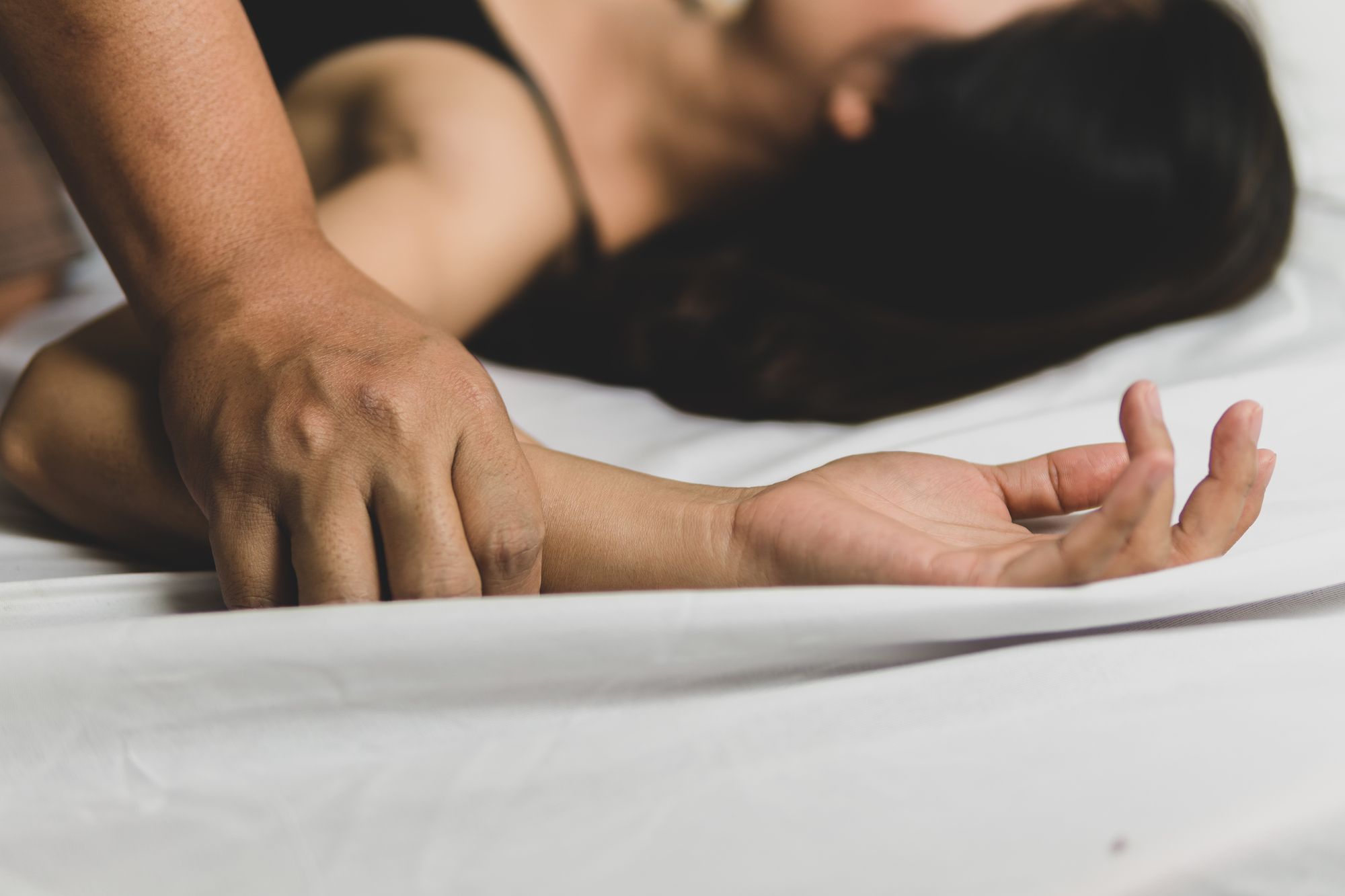 ベッドに横たわる女性と、女性の手を鷲掴みにする男性の手