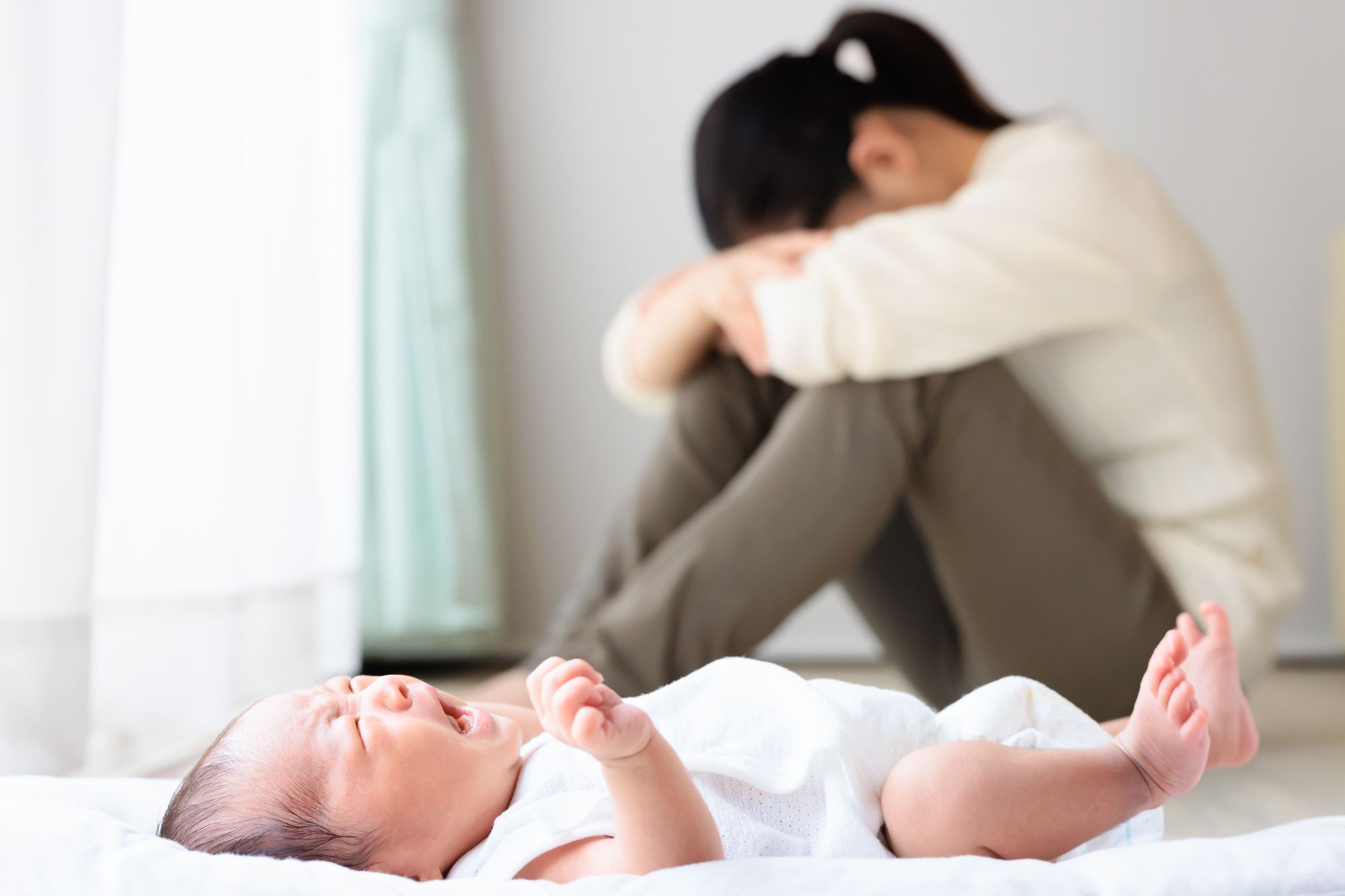 泣いている赤ちゃんと膝を抱えてうつむく女性